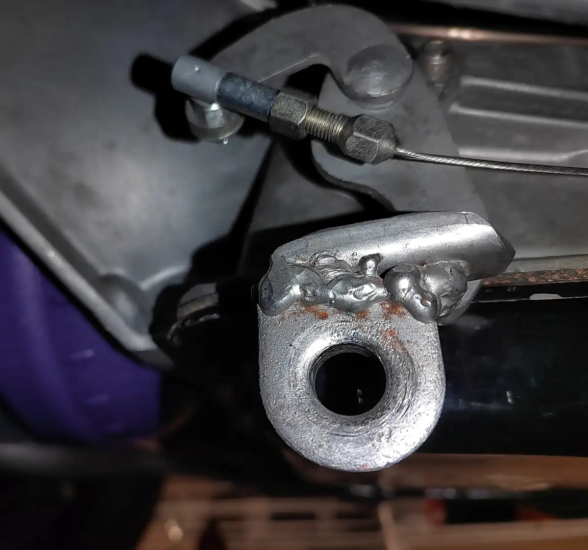A close-up photo shows a metal bike part, likely a brake or suspension component, with a crude, lumpy weld job shaped like a…