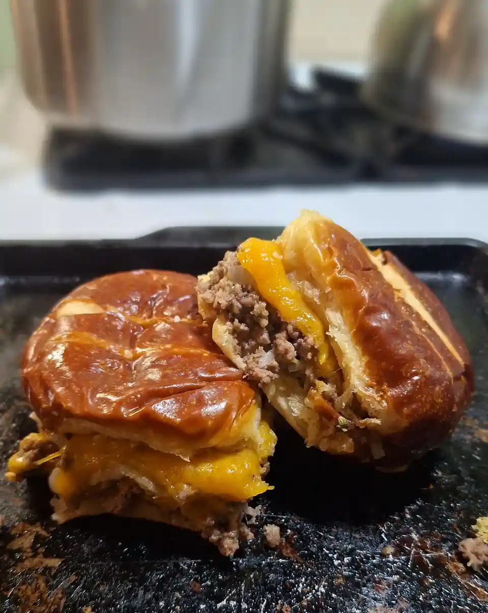 A close-up photo shows a cheeseburger, split in half, revealing melted yellow cheese and browned ground meat inside a…
