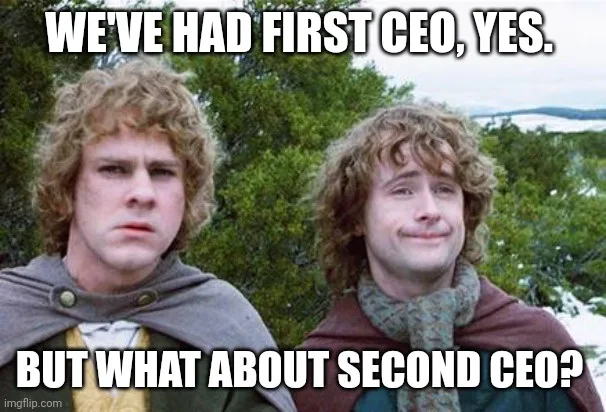 Two identical-looking men with curly hair stand side by side outdoors. The man on the left has a skeptical, unimpressed…