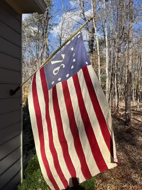 An American flag with red and white stripes and a blue canton featuring stars, but with a white scissor symbol replacing the…