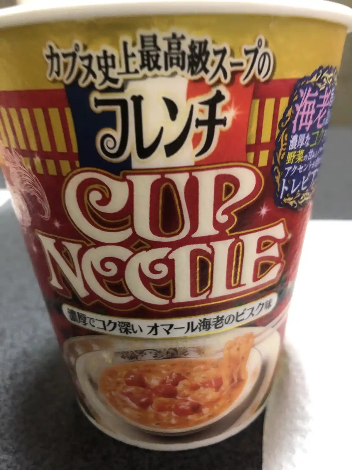 A close-up photo of a Japanese Cup Noodle cup with ornate, luxurious packaging. The label features large text proclaiming it…