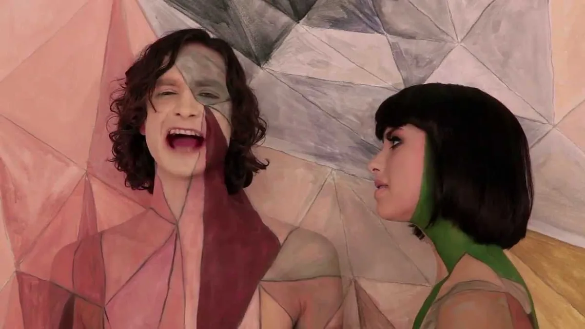 A man and a woman are depicted in a stylized, geometrically segmented painting. The man, on the left, has his face split…