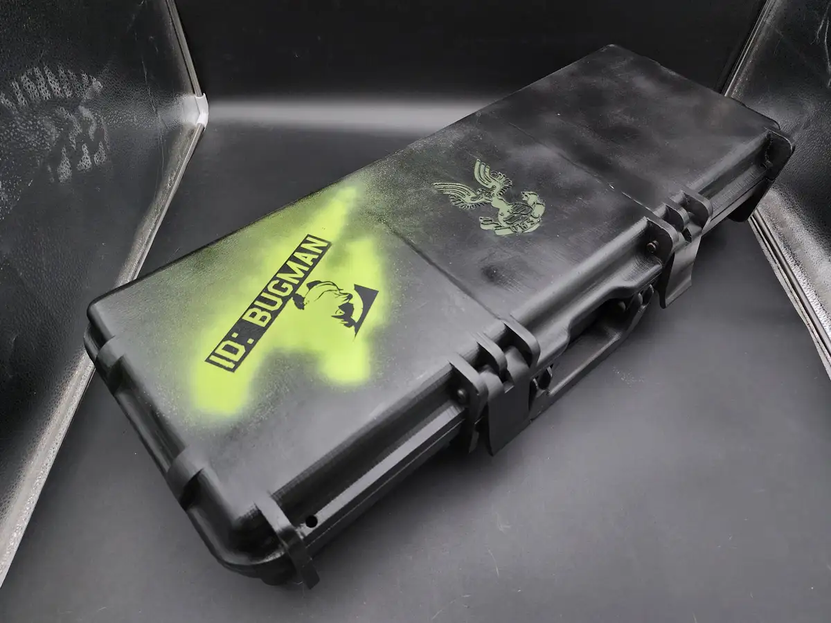 A black, rugged, rectangular case with a greenish-yellow spray-painted section featuring the text 'ID: BUGMAN' and a…