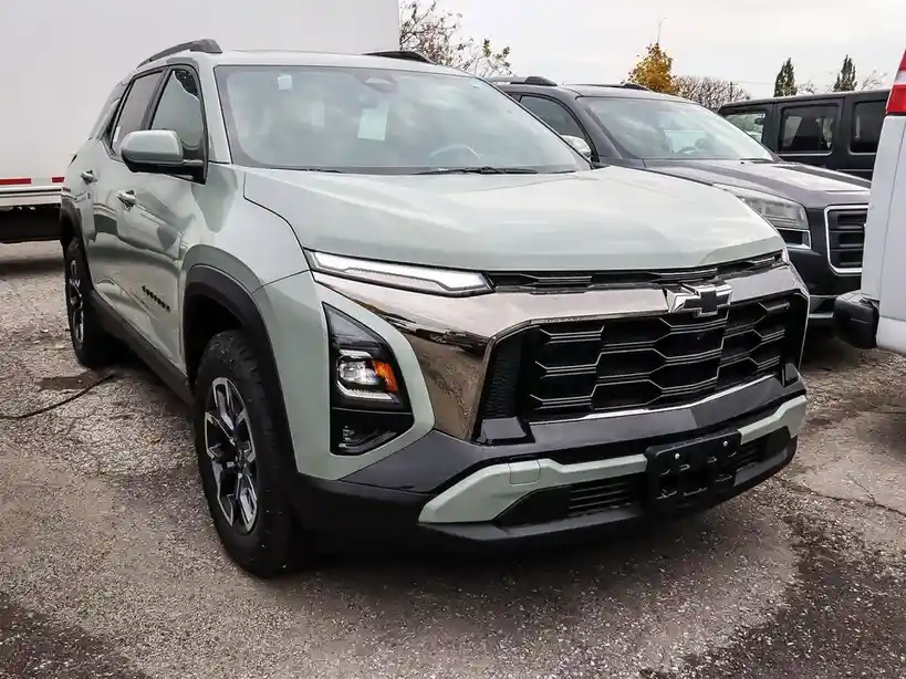 a light green chevrolet blazer suv is parked in a lot with other vehicles visible in the background. the car's front grille…