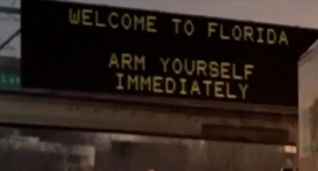 A dark electronic highway sign displays the text 'WELCOME TO FLORIDA' on the top line and 'ARM YOURSELF IMMEDIATELY' on the…