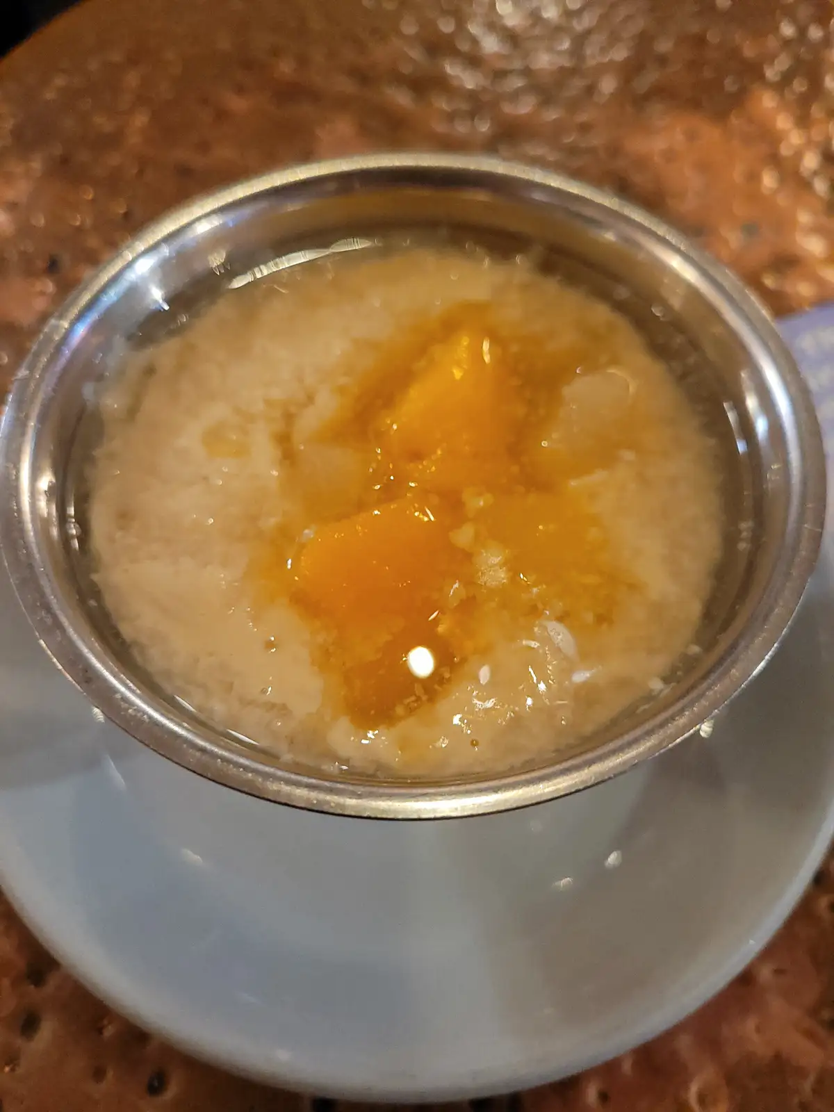A close-up photo shows a small metal bowl filled with a light-colored, grainy liquid topped with several bright orange…