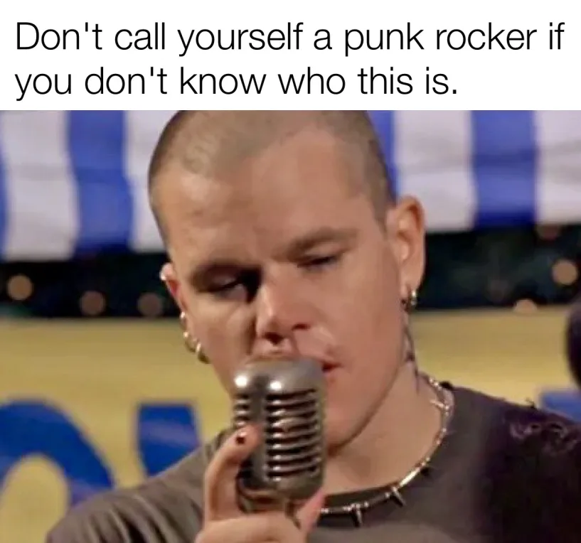 A close-up image of a man with a shaved head, wearing multiple earrings and a spiked choker, singing into a vintage-style…