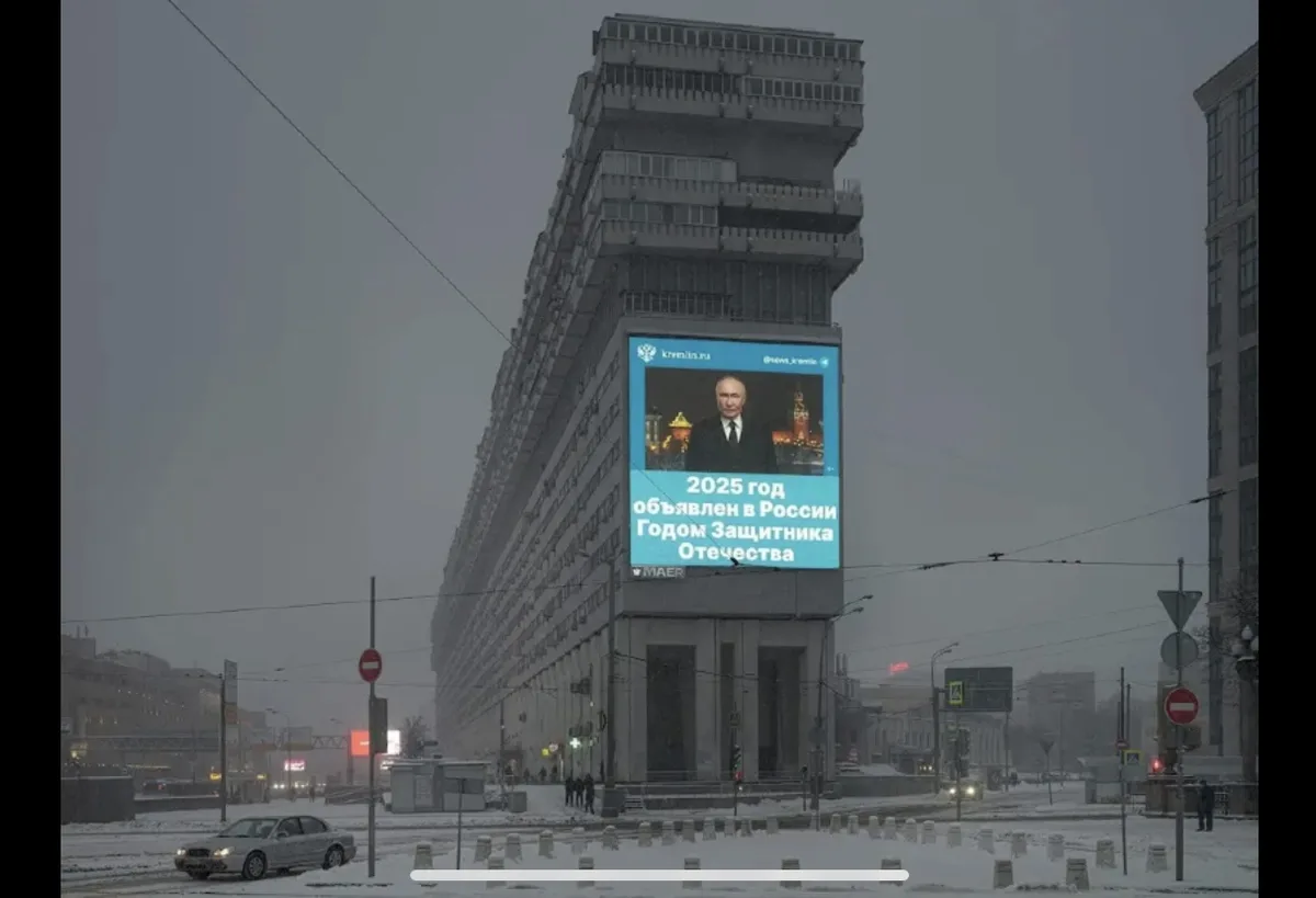 A large digital billboard on a snowy, overcast urban street displays a photo of Vladimir Putin with Russian text declaring…