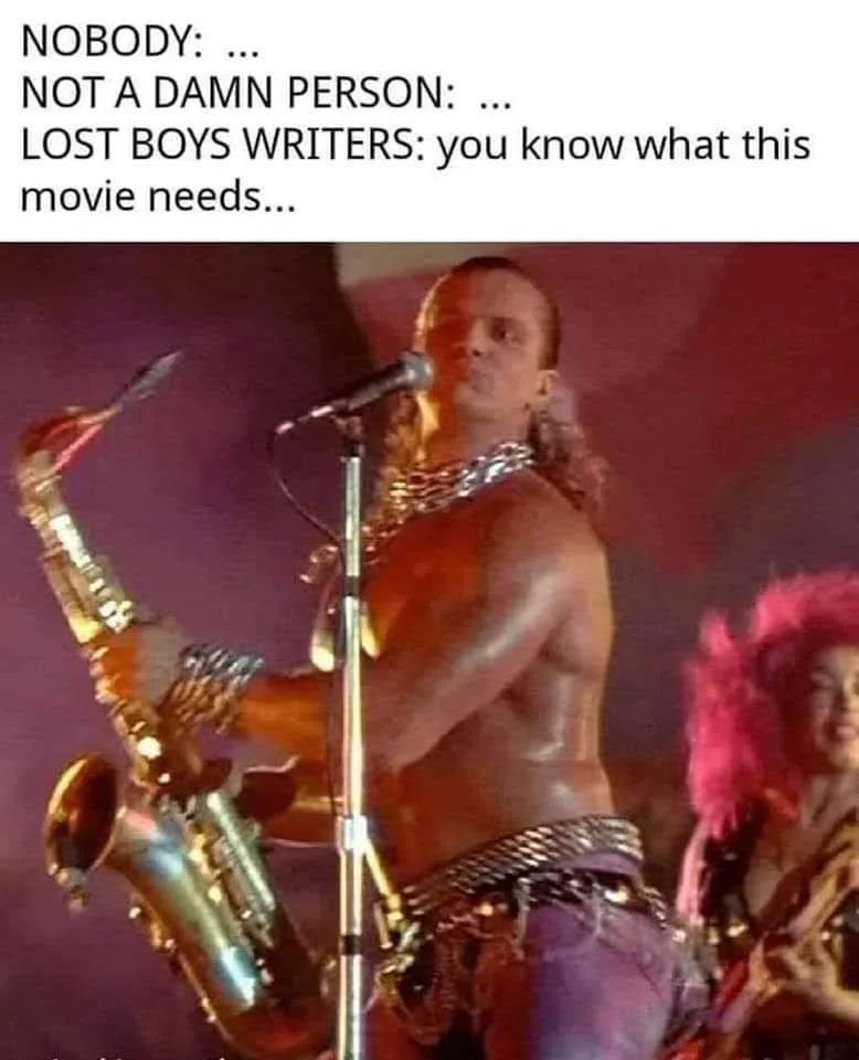 A shirtless man with long hair and chains plays a saxophone on stage while another person with pink hair is partially…