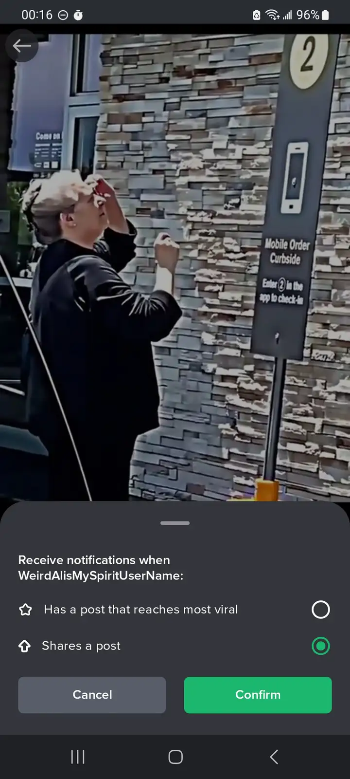 A person stands at a curbside pickup station marked with a sign that says 'Mobile Order Curbside' and 'Enter 2 in the app to…