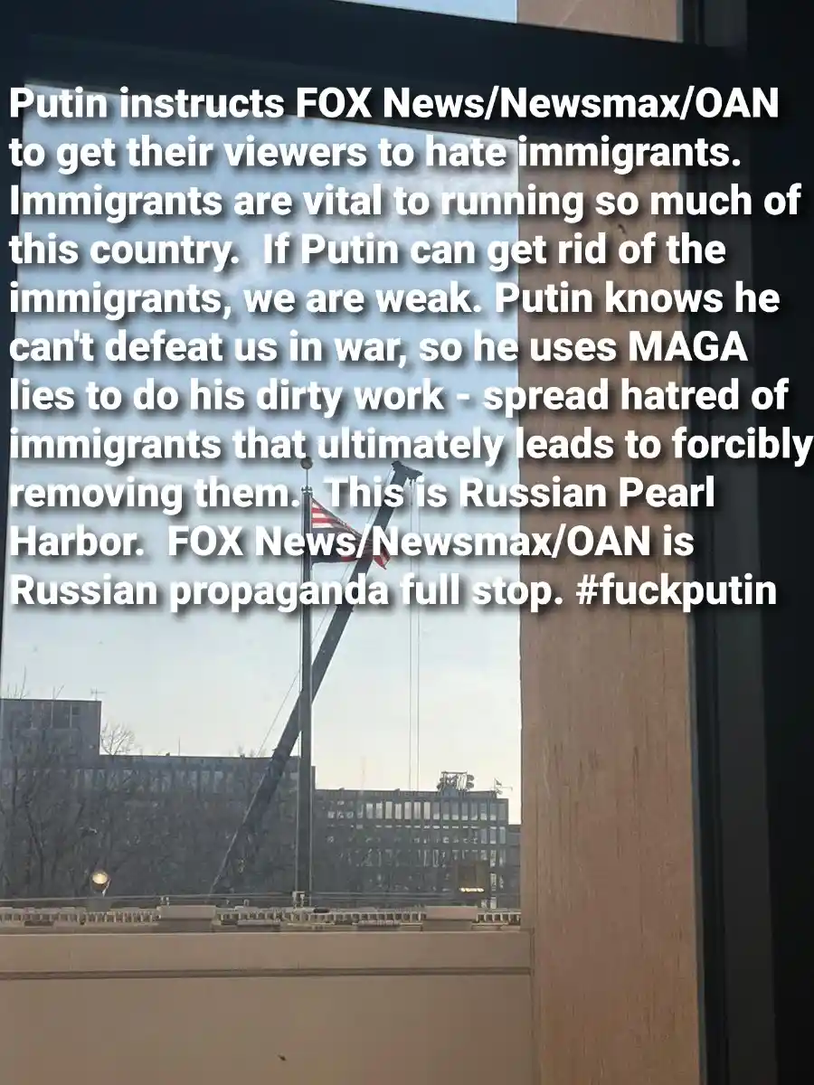 A photo taken from inside a building looking out a window at an American flag on a pole, with a crane visible in the…