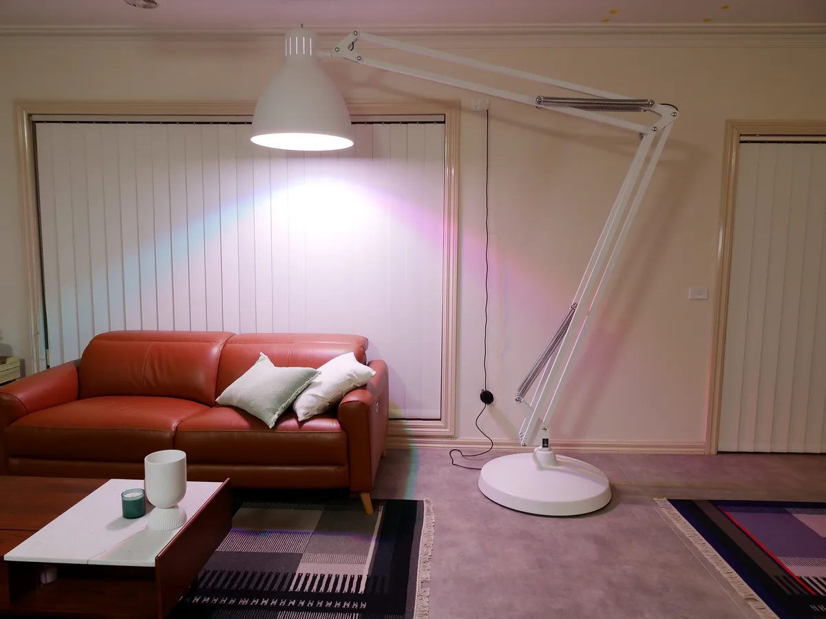 A large white articulated floor lamp is positioned in a living room, casting a bright, colorful rainbow-like light onto the…