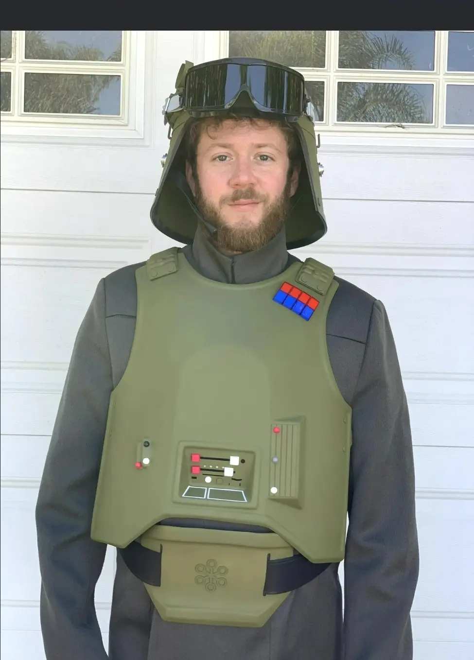 A man with a beard stands in front of a white garage door wearing a full stormtrooper costume, including the helmet with…