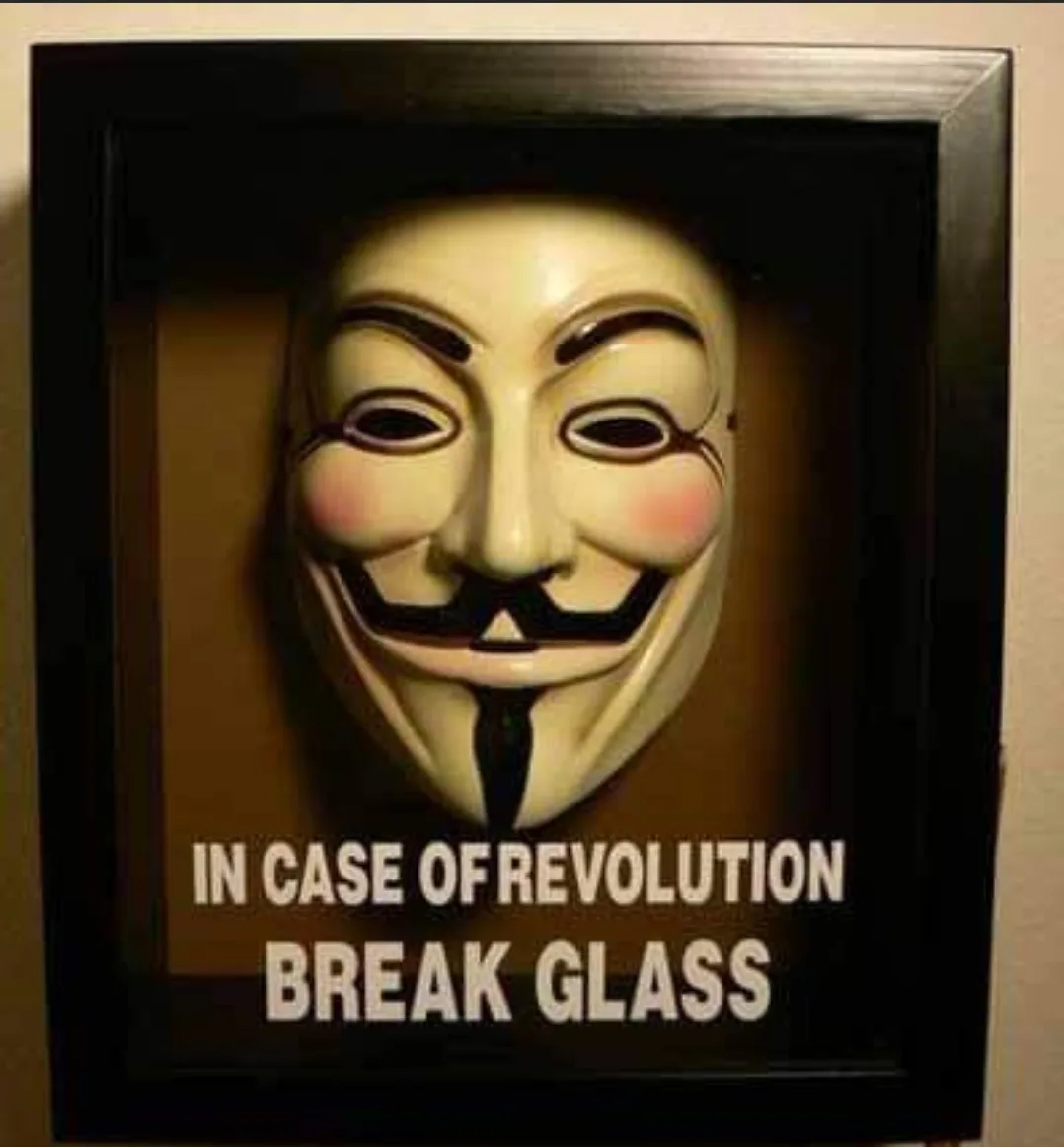 A framed picture displays a white Guy Fawkes mask, commonly associated with the Anonymous movement, mounted behind glass…