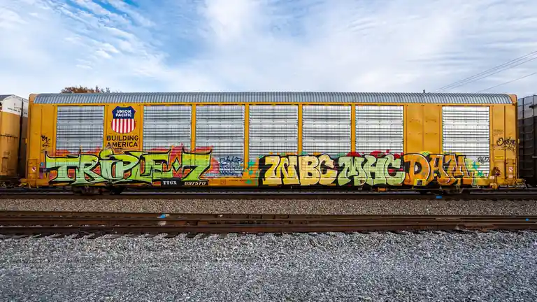 A yellow Union Pacific freight train car with 'BUILDING AMERICA' branding is covered in colorful graffiti, including the…