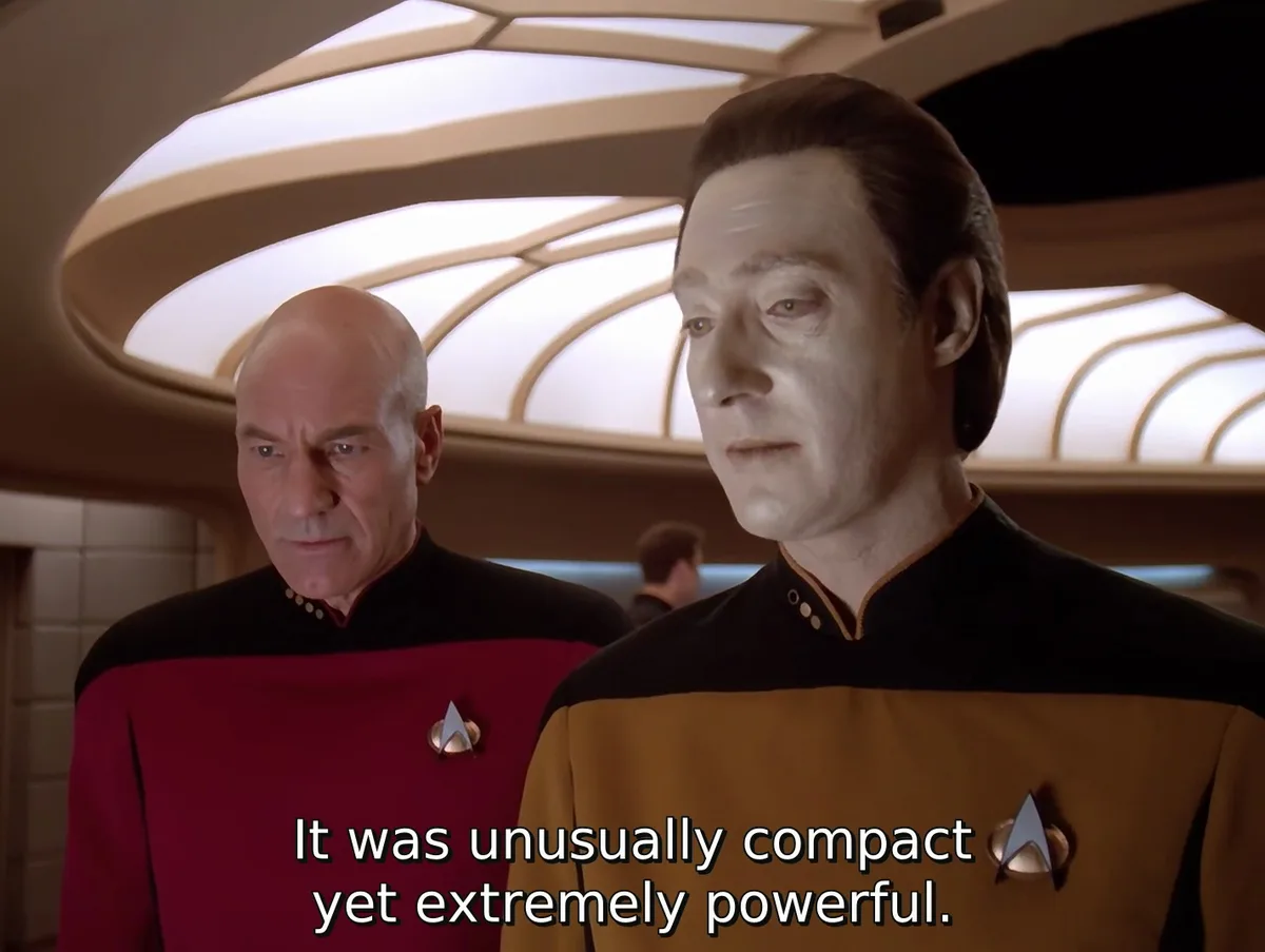 Two men in Starfleet uniforms stand in a spaceship corridor, one in a red shirt and one in a gold shirt. The man in the gold…