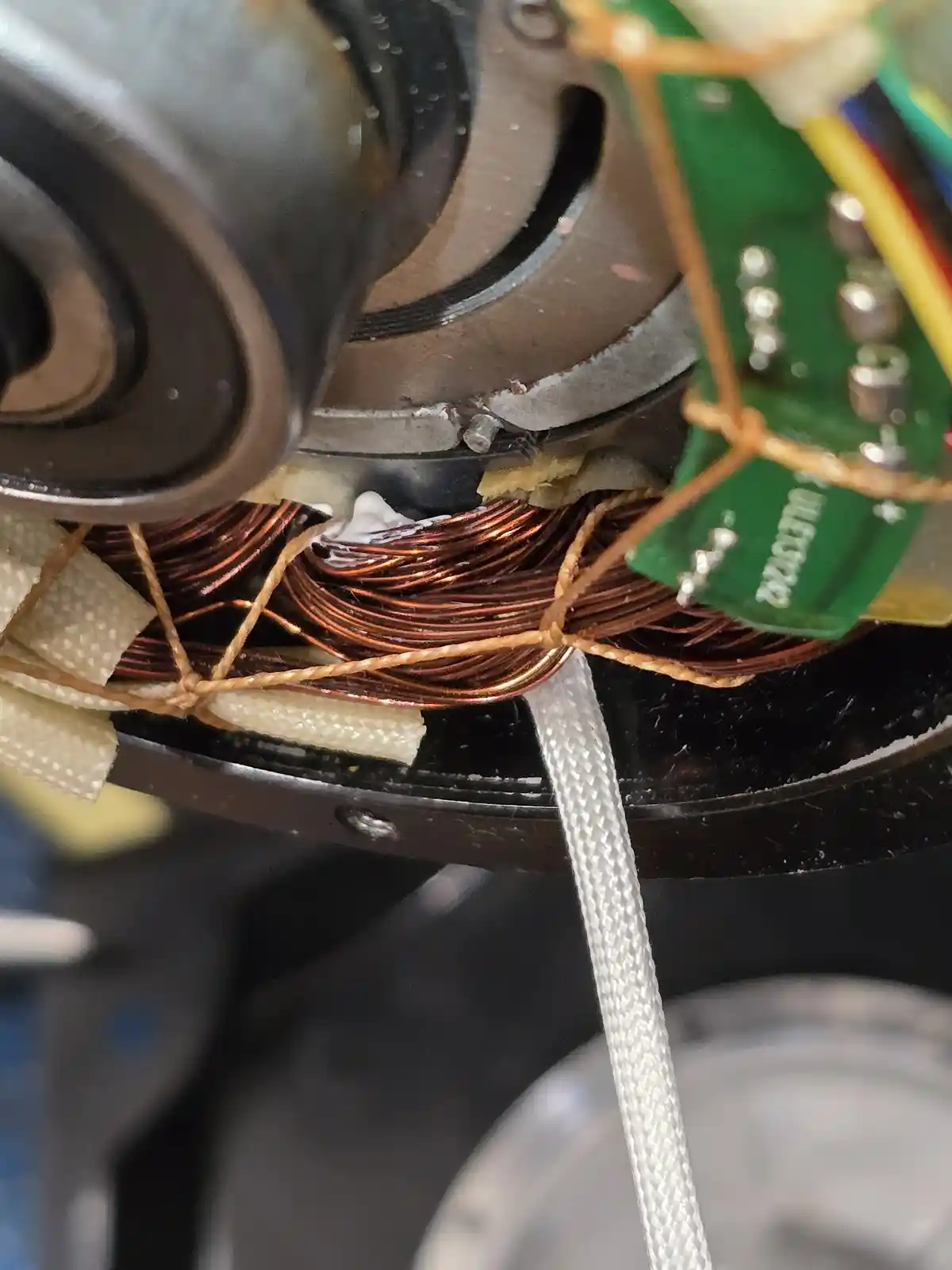 A close-up photo of a disassembled electronic device's internal components, showing copper wire coils, a green circuit…