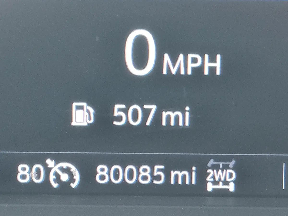 A close-up of a car's digital dashboard showing 0 MPH speed, 507 miles of fuel range, 80°F temperature, and 80,085 miles…