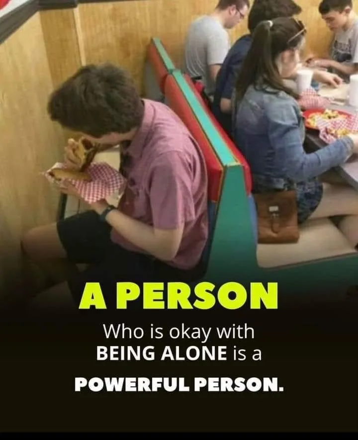 A young man in a pink shirt sits alone in a diner booth, eating a sandwich while others sit at adjacent tables. The text…