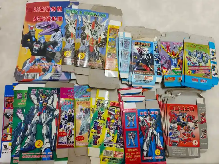 An overhead shot displays numerous open cardboard boxes of Taiwanese toy robot kits, featuring colorful illustrations of…