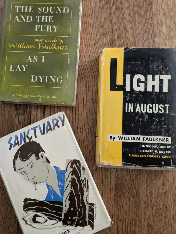 Three vintage William Faulkner books — 'The Sound and the Fury' and 'As I Lay Dying' in a green cover, 'Light in August' in…