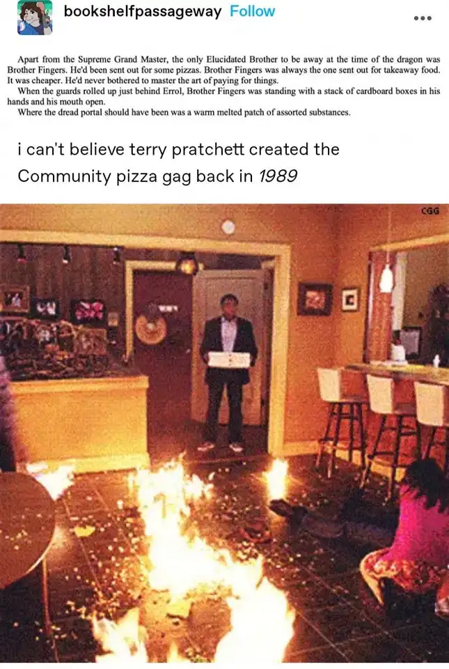 A man in a suit stands in a doorway holding a pizza box, while a large fire burns on the floor in front of him. A woman in a…