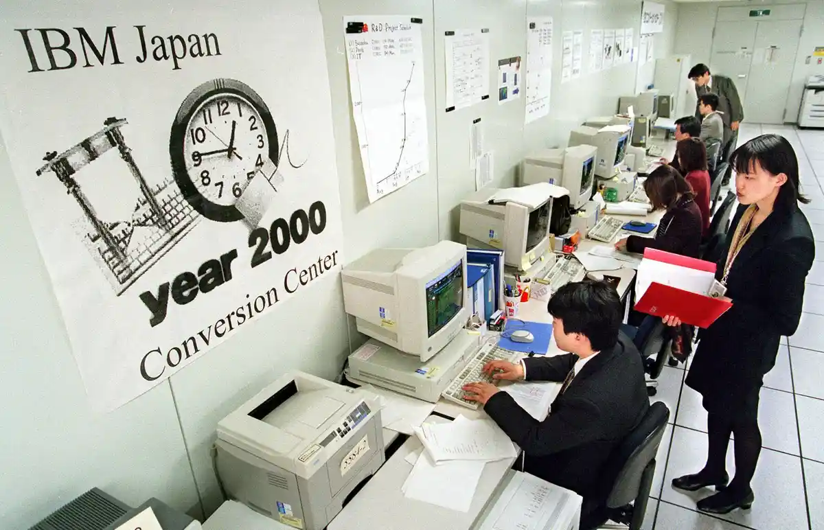 An IBM Japan office with employees working at computers, a large banner reads 'IBM Japan year 2000 Conversion Center' with a…
