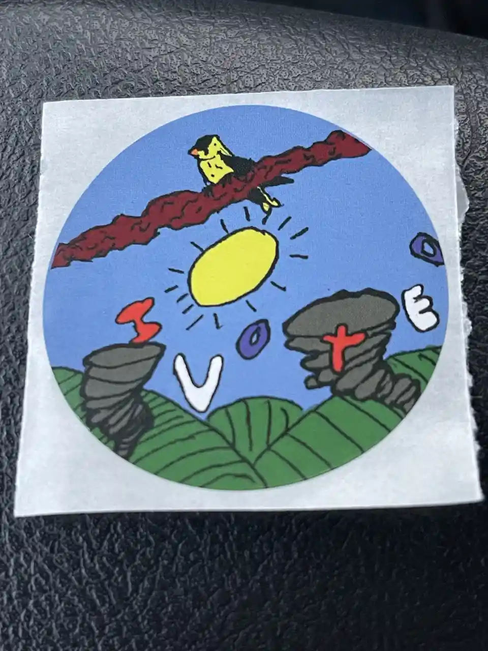 A hand-drawn circular sticker depicts a yellow bird perched on a red branch above a yellow sun, with the letters 'I', 'V'…