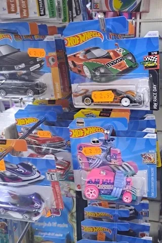 A retail display of Hot Wheels toy cars in their original blister packaging, arranged on shelves. Each package has a yellow…